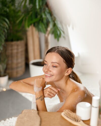 joyful-young-woman-smiling-away-and-leaning-on-bathtub-side-while-bathing-at-spa-resort.jpg